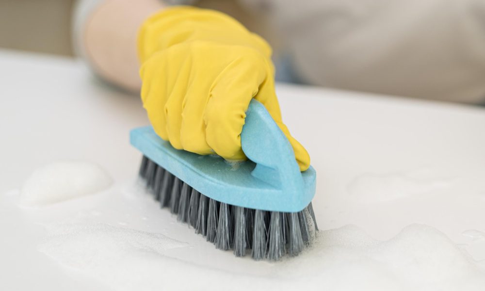 Main gantée en utilisant une brosse pour nettoyer une surface.