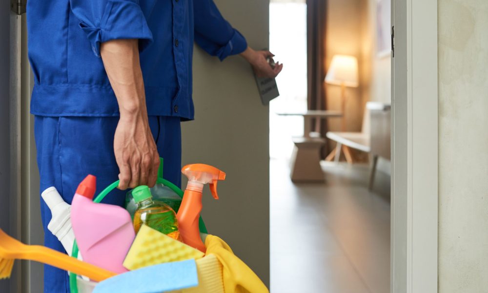 Agent de nettoyage entrant dans une pièce avec des produits d'entretien.